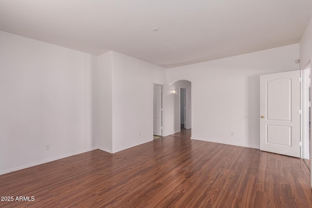empty room with arched walkways, baseboards, and wood finished floors