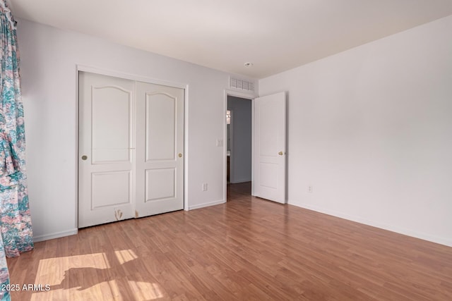 unfurnished bedroom with visible vents, light wood finished floors, baseboards, and a closet