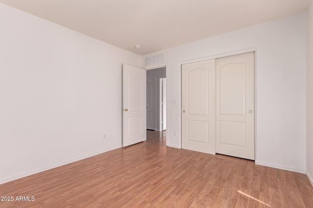 unfurnished bedroom with baseboards, a closet, light wood finished floors, and visible vents