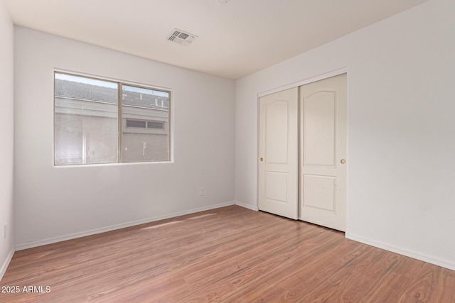 unfurnished bedroom with baseboards, a closet, light wood-type flooring, and visible vents