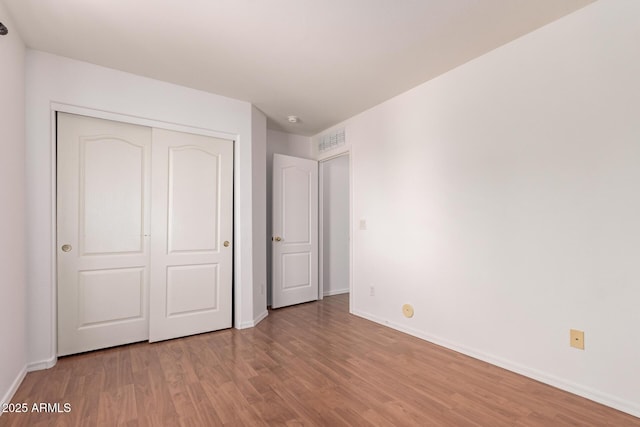 unfurnished bedroom featuring baseboards, visible vents, wood finished floors, and a closet
