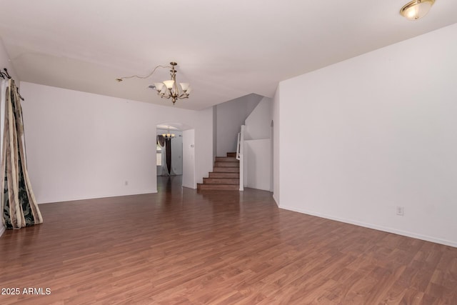 unfurnished living room with stairs, an inviting chandelier, and wood finished floors