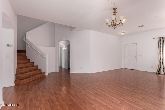 unfurnished living room featuring arched walkways, wood finished floors, a chandelier, and visible vents