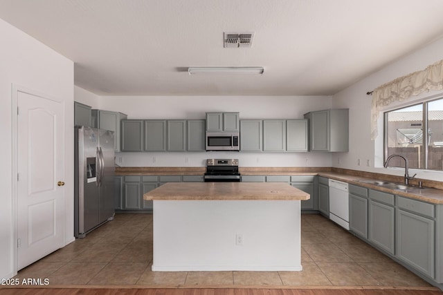 kitchen featuring stainless steel appliances, light tile patterned flooring, a sink, and gray cabinets