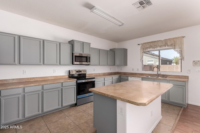 kitchen featuring stainless steel appliances, gray cabinetry, a sink, and visible vents
