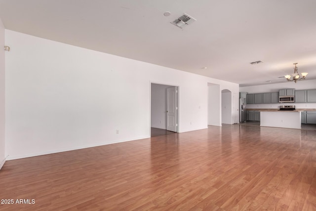 unfurnished living room with arched walkways, visible vents, light wood-type flooring, and a notable chandelier