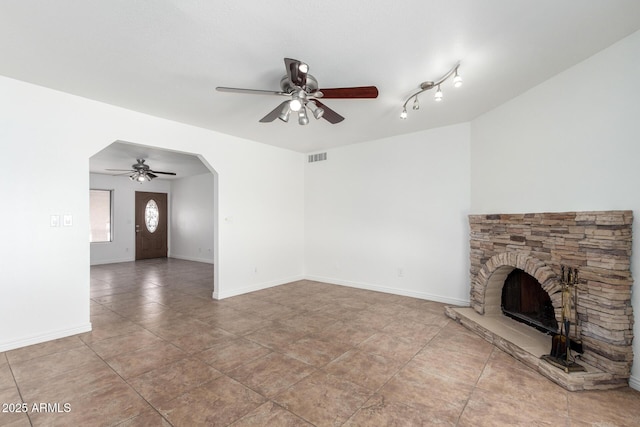 unfurnished living room featuring tile patterned floors, visible vents, a stone fireplace, and a ceiling fan
