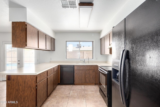 kitchen featuring a sink, light countertops, a peninsula, black appliances, and light tile patterned flooring