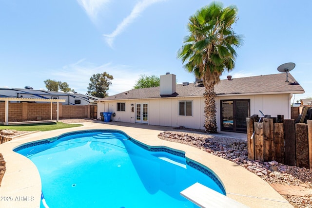 view of swimming pool featuring a fenced in pool, a diving board, french doors, a patio area, and a fenced backyard