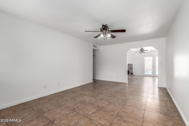 empty room featuring baseboards, tile patterned floors, visible vents, ceiling fan, and arched walkways