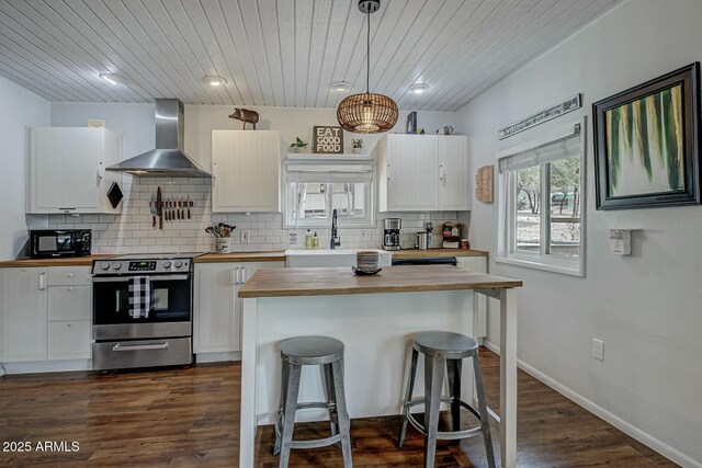 kitchen with butcher block counters, white cabinets, wall chimney range hood, stainless steel range with electric stovetop, and black microwave