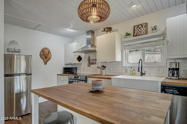 kitchen featuring decorative backsplash, butcher block counters, appliances with stainless steel finishes, wall chimney range hood, and a sink