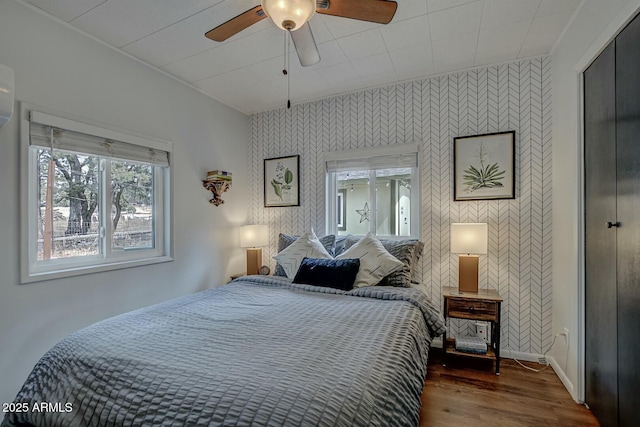 bedroom with baseboards, ceiling fan, wood finished floors, and wallpapered walls