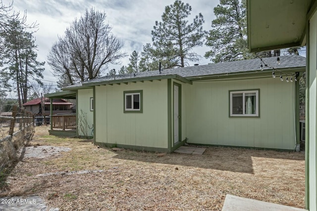 rear view of property featuring a shingled roof and fence