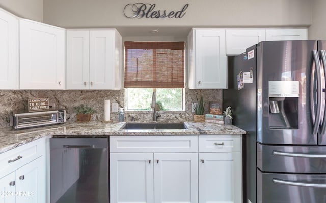 kitchen with light stone counters, stainless steel appliances, white cabinetry, and sink