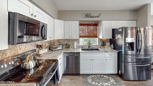 kitchen featuring appliances with stainless steel finishes, light stone counters, white cabinetry, and sink