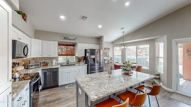 kitchen with stainless steel appliances, light hardwood / wood-style floors, a kitchen island, hanging light fixtures, and lofted ceiling