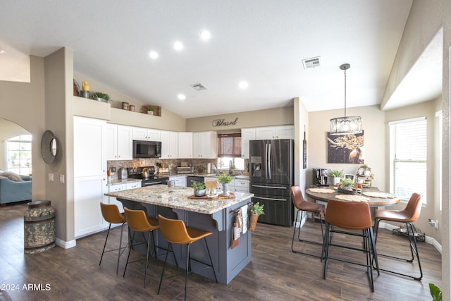 kitchen with white cabinets, dark hardwood / wood-style floors, light stone countertops, decorative light fixtures, and stainless steel appliances