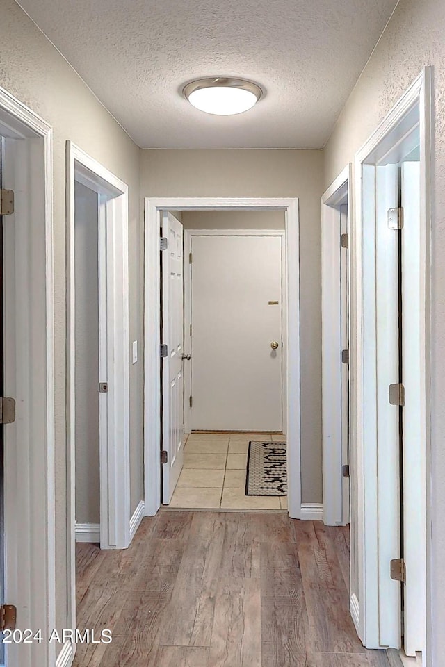 corridor with a textured ceiling and light wood-type flooring