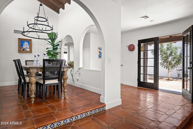 dining space with beamed ceiling, an inviting chandelier, dark tile patterned flooring, and french doors