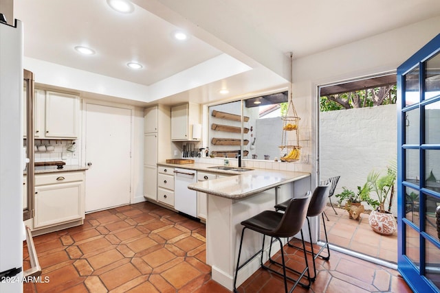 kitchen featuring tasteful backsplash, kitchen peninsula, white dishwasher, a breakfast bar area, and white cabinets