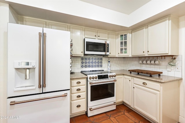 kitchen featuring dark tile patterned flooring, light stone countertops, white appliances, and tasteful backsplash