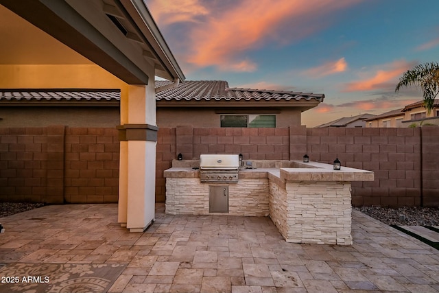 patio terrace at dusk with area for grilling, a grill, and fence