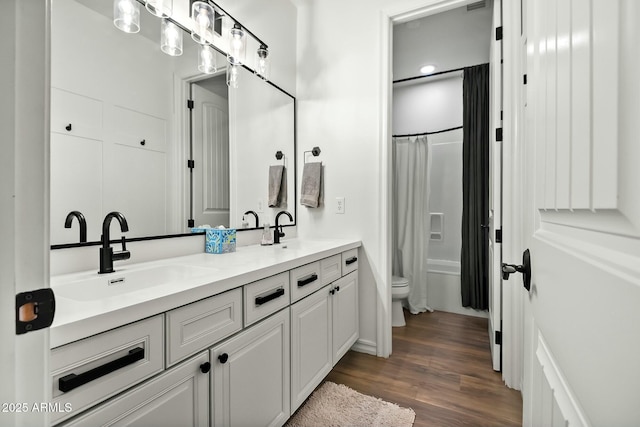 full bath with double vanity, wood finished floors, a sink, and toilet