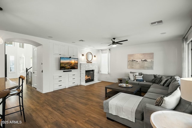 living room with visible vents, arched walkways, dark wood-style flooring, a fireplace, and a wealth of natural light