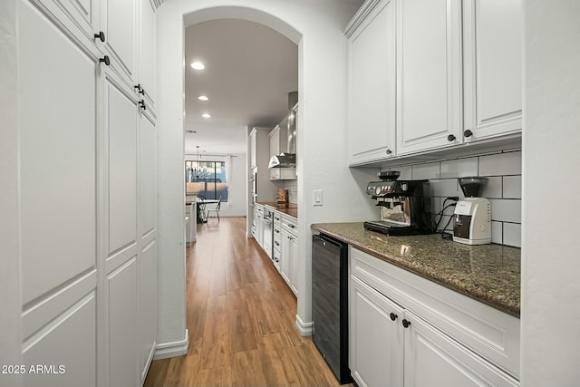 kitchen featuring arched walkways, recessed lighting, beverage cooler, white cabinetry, and light wood finished floors