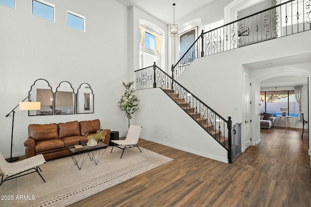 living area featuring a notable chandelier, stairway, a high ceiling, wood finished floors, and baseboards