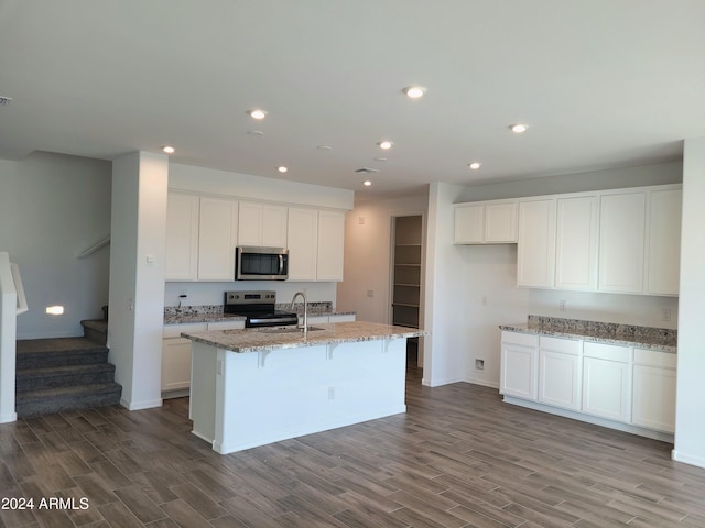 kitchen with stainless steel appliances, light stone counters, wood-type flooring, a center island with sink, and white cabinets