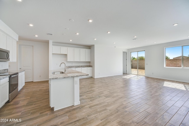 kitchen with appliances with stainless steel finishes, white cabinetry, a kitchen island with sink, and light stone counters