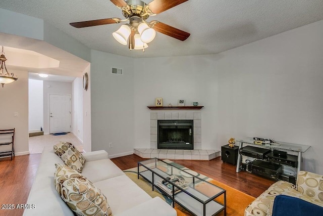 living room with ceiling fan, a tiled fireplace, hardwood / wood-style floors, and a textured ceiling