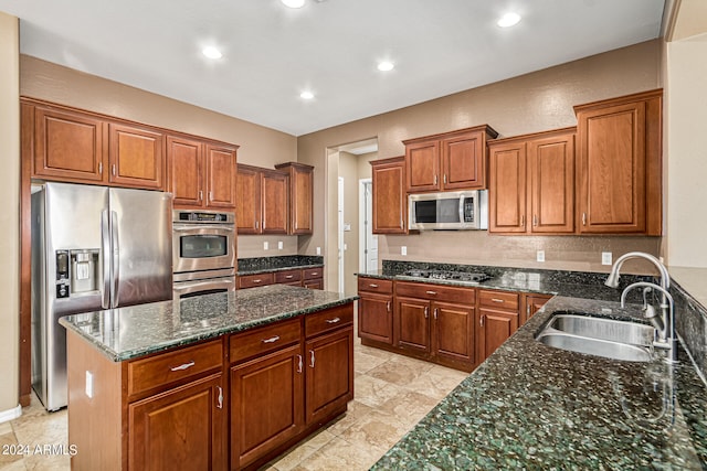 kitchen with appliances with stainless steel finishes, a kitchen island, dark stone countertops, and sink