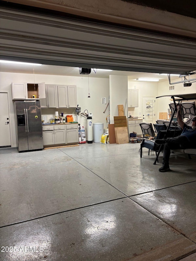 garage featuring visible vents, a garage door opener, and stainless steel refrigerator with ice dispenser