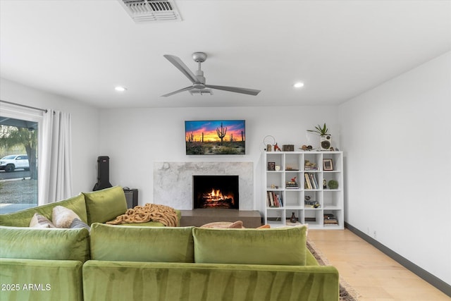 living room with light wood finished floors, recessed lighting, visible vents, a high end fireplace, and baseboards