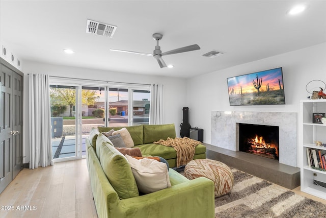 living room with light wood-type flooring, recessed lighting, visible vents, and a high end fireplace