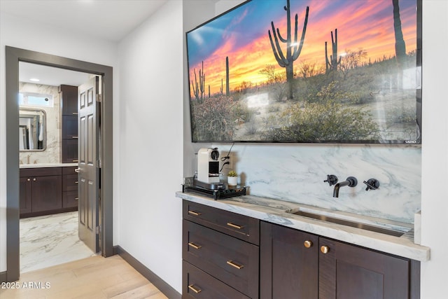 bar featuring baseboards, a sink, light wood finished floors, and decorative backsplash