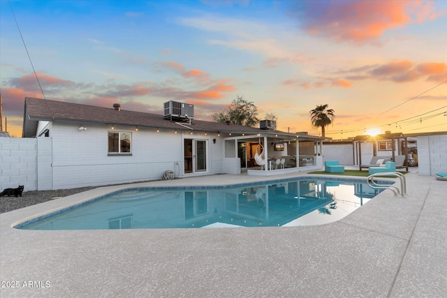 pool at dusk featuring central AC, a patio area, fence, and a fenced in pool