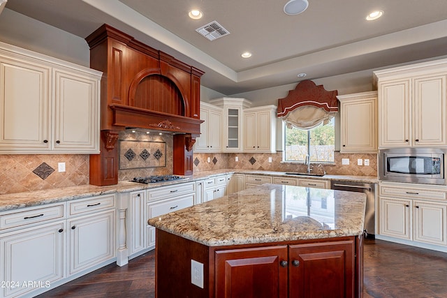 kitchen with appliances with stainless steel finishes, backsplash, dark wood-type flooring, sink, and a center island