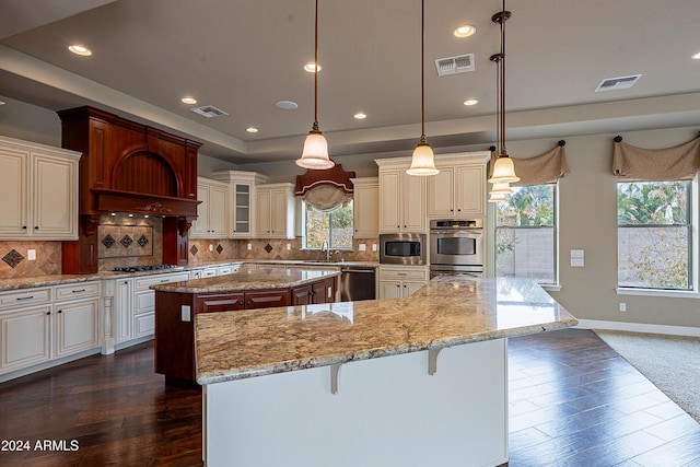 kitchen with a center island, backsplash, dark wood-type flooring, hanging light fixtures, and appliances with stainless steel finishes