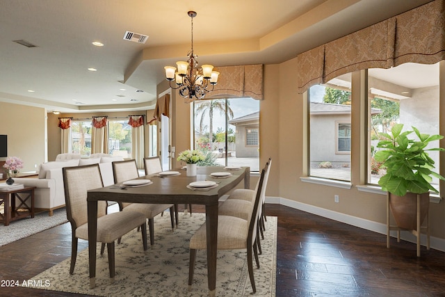 dining room with a notable chandelier, plenty of natural light, dark wood-type flooring, and a tray ceiling