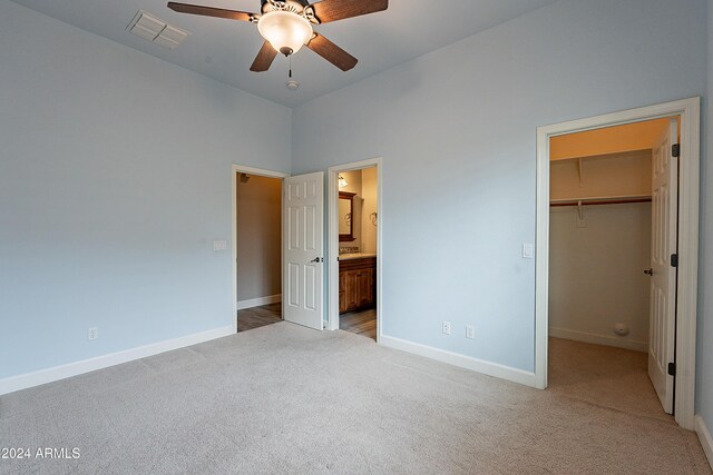 unfurnished bedroom featuring ceiling fan, ensuite bathroom, a walk in closet, light carpet, and a closet