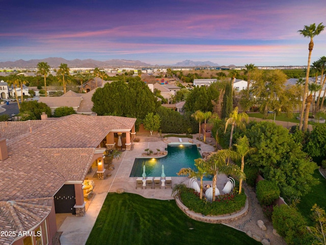 pool at dusk featuring a patio, a mountain view, fence, a residential view, and an outdoor pool