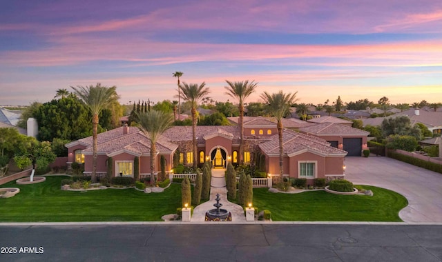 mediterranean / spanish-style home featuring concrete driveway, a lawn, an attached garage, and stucco siding