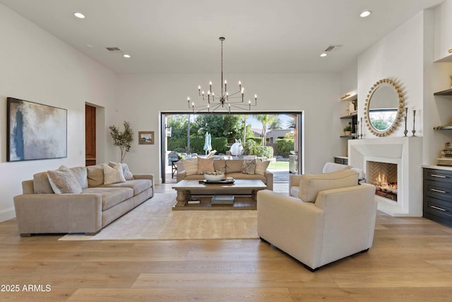 living area with built in features, a lit fireplace, a chandelier, and light wood-style flooring