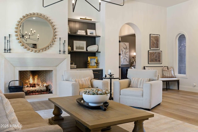 living area with a towering ceiling, a warm lit fireplace, arched walkways, and wood finished floors