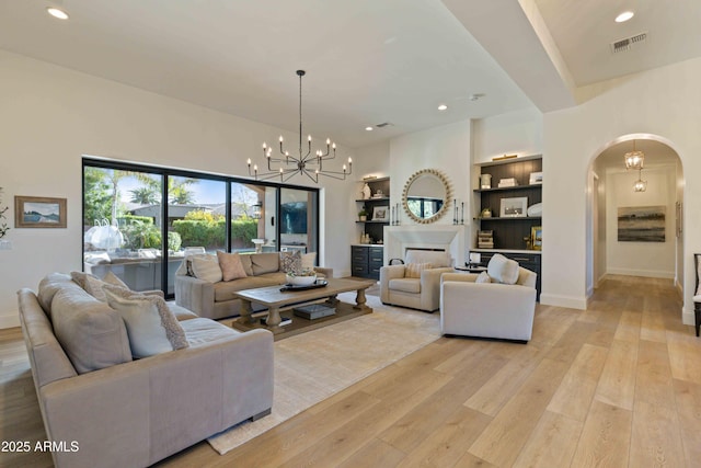 living room with light wood-style floors, arched walkways, visible vents, and a fireplace