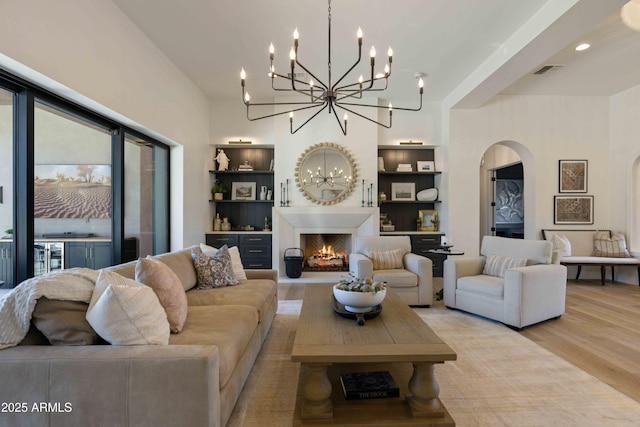 living area with a warm lit fireplace, light wood finished floors, visible vents, arched walkways, and built in shelves